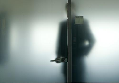 A man in a suit, seen as a blurred silhouette through frosted glass, holding a door handle